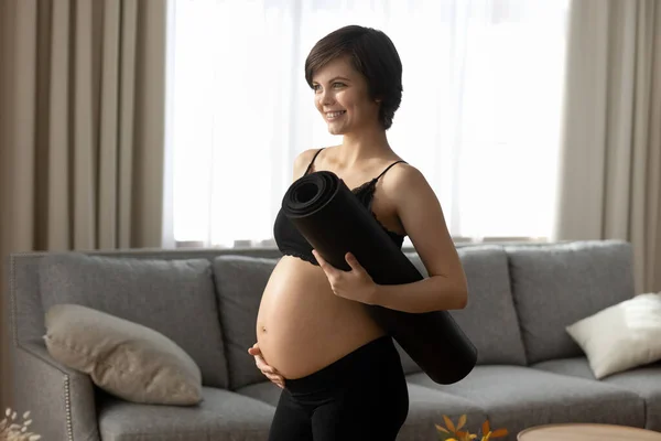 Smiling pregnant woman in black sportswear holding yoga mat — Stock Photo, Image