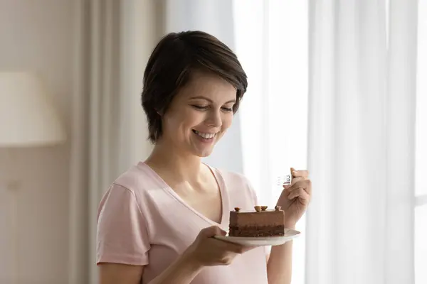 Крупным планом улыбающаяся красивая женщина ест торт, наслаждаясь десертом — стоковое фото