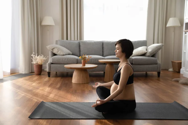 Vista lateral mujer embarazada en ropa deportiva negro meditando en casa — Foto de Stock