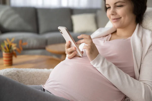 Close up agradável mulher grávida usando smartphone, se divertindo online — Fotografia de Stock