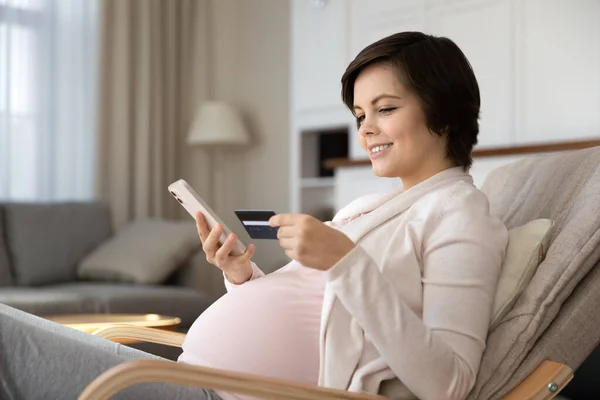 Sorrindo mulher grávida pagando on-line por cartão de crédito, usando telefone — Fotografia de Stock