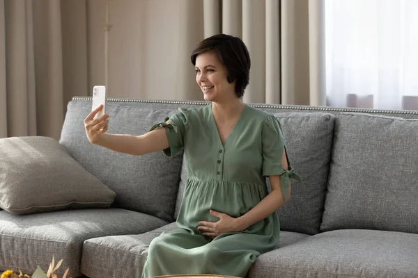 Usmívající se těhotná žena drží smartphone, dělat videohovor doma — Stock fotografie