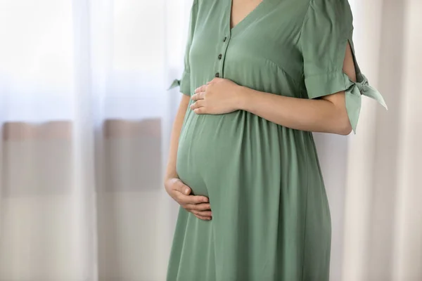 Närbild beskärs gravid kvinna i grön klänning röra magen — Stockfoto