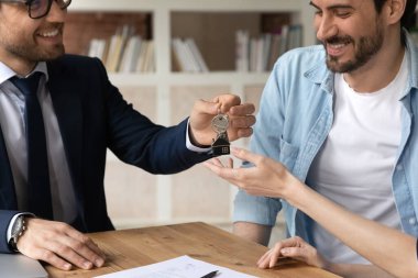 Gülümseyen genç emlakçı mutlu müşterilere anahtar veriyor..