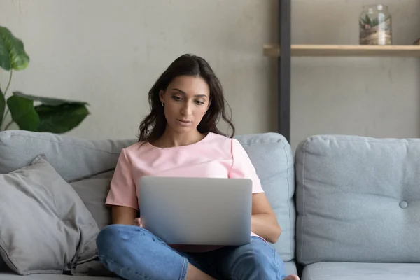 Kendine güvenen Arap bir kadın dizüstü bilgisayarla koltukta oturuyor, internette çalışıyor. — Stok fotoğraf