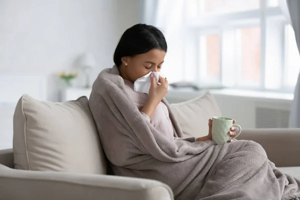 Frustrated sick mixed raced woman wrapped in warm blanket — Stock Photo, Image