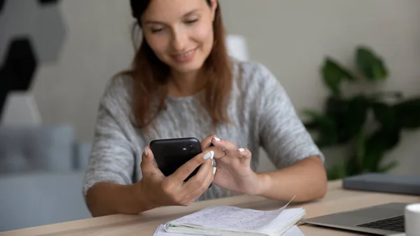 Cerca de la mujer sonriente usando el teléfono inteligente, sentado en el escritorio —  Fotos de Stock