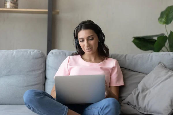 Arabo donna in cuffia utilizzando il computer portatile, seduto sul divano — Foto Stock