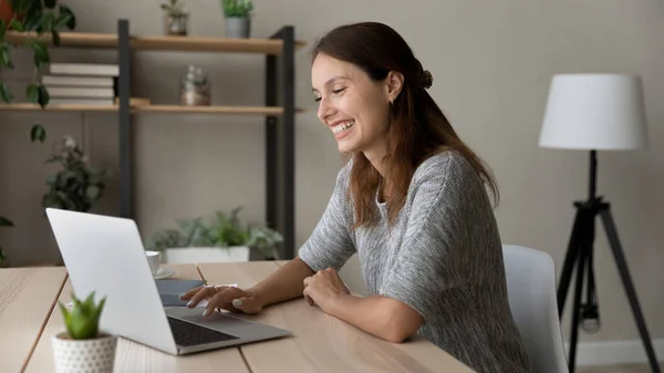 Femme souriante utilisant un ordinateur portable, assise au bureau, s'amusant — Photo