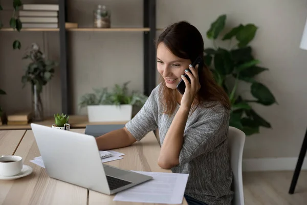 Glimlachende vrouw aan het bellen, kijkend naar laptop scherm — Stockfoto