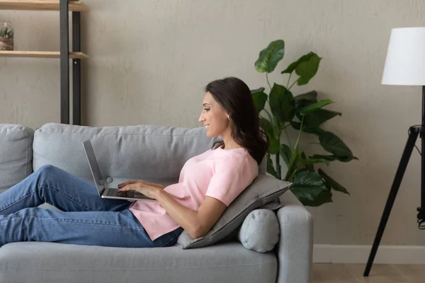 Vista lateral sorrindo mulher árabe usando laptop, relaxante no sofá — Fotografia de Stock