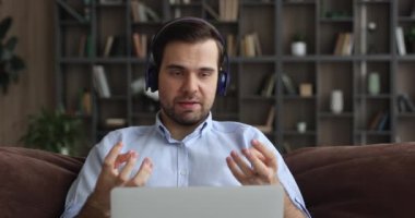 Kulaklık takan bir adam kanepede dizüstü bilgisayarla oturur ve video görüşmesi yapar.