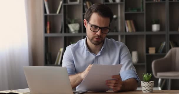 Empresário lendo papéis contratuais enquanto se senta no local de trabalho no escritório — Vídeo de Stock