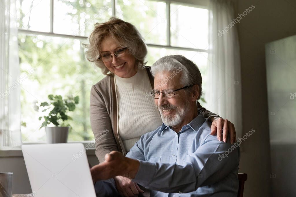 Smiling senior couple use computer together at home