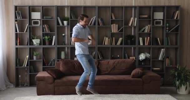 Szczęśliwy młody człowiek taniec w salonie relaks na kanapie — Wideo stockowe