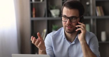 Adam modern işyerinde oturup müşteriyle telefonda konuşuyor.