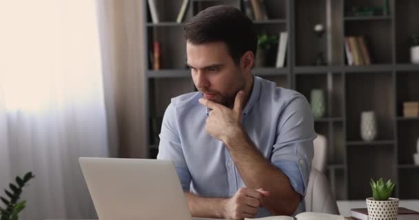Düşünceli bir çalışan çalışma masasında oturup bilgisayar üzerinde çalışıyor. — Stok video