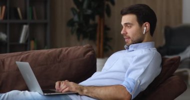 Adam kanepeye oturup video konferans uygulaması ile bilgisayarla konuşuyor.