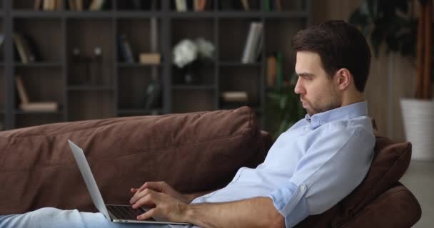 Sério focado homem sentado no sofá confortável com laptop — Vídeo de Stock