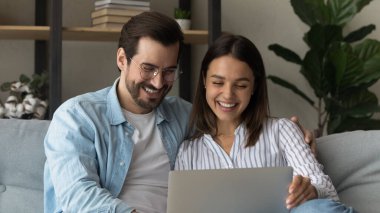 Laughing happy young couple using computer at home.