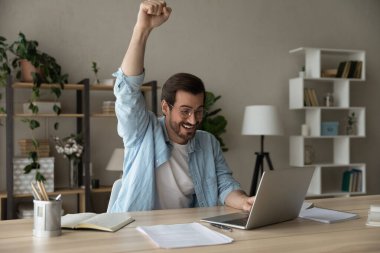 Emotional young man celebrating internet success at home.