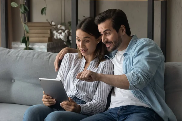 Surprised young happy couple looking at digital computer tablet.