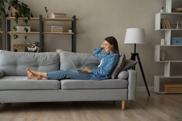 Расслабленная улыбающаяся женщина тысячелетия, пользующаяся компьютером дома.