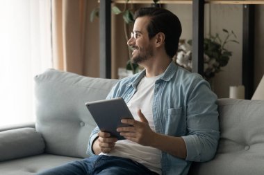 Happy dreamy young man holding digital tablet in hands.