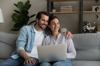 Happy dreamy bonding young family couple using computer.