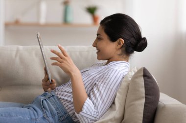 Genç Hintli kadın kanepede tabletle dinleniyor.