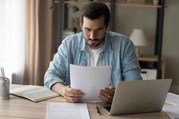 Concentrated young man in glasses looking through paper correspondence. — Stock Photo, Image