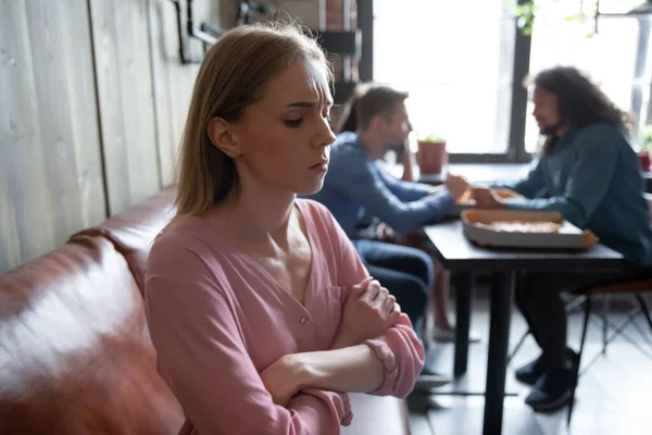 Unhappy abused young woman sitting separately from friends in cafe. — Stok fotoğraf