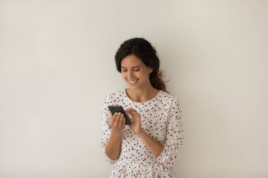 Akıllı telefon kullanan gülümseyen kadın, gri duvar arkasında duruyor.