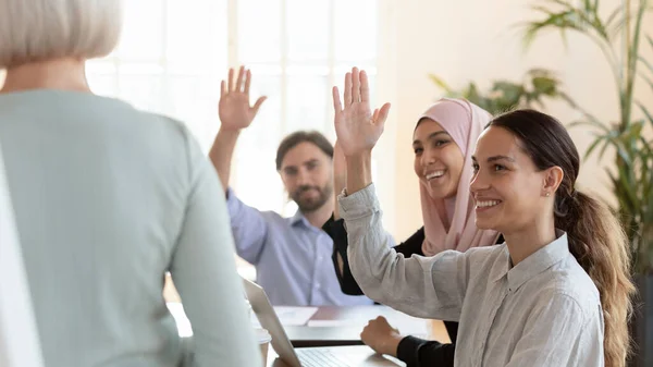 Smiling diverse employees with raised hands voting at meeting