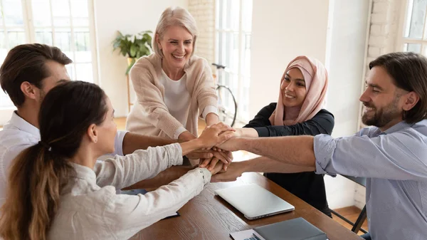 Opgewonden glimlachende multi-etnische medewerkers team stapelen handen op de vergadering — Stockfoto