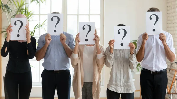 Verscheidene zakenmensen verbergen gezichten achter kranten met vraagtekens — Stockfoto