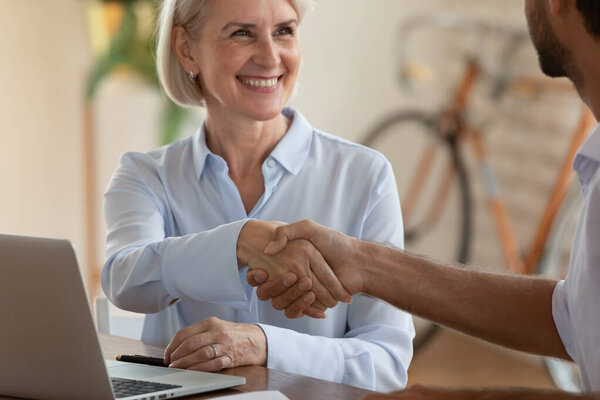 Smiling middle aged manager shaking client hand at meeting