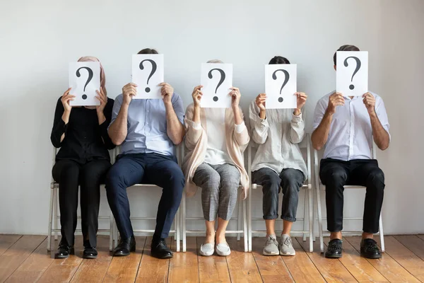 Diversos candidatos de trabajo escondiendo caras detrás de hojas con signos de interrogación —  Fotos de Stock