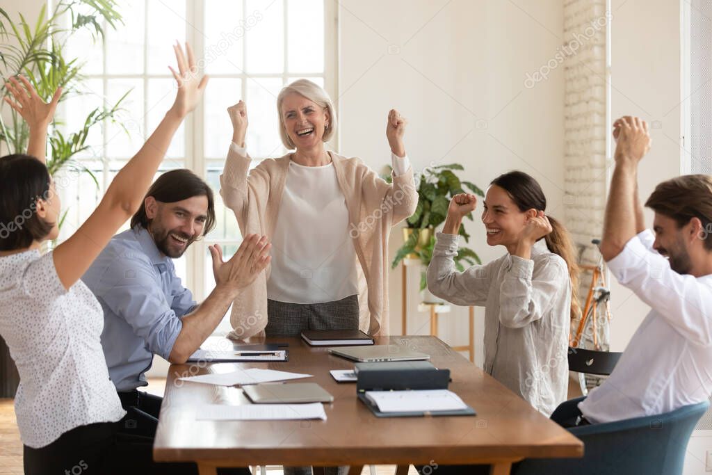 Excited diverse employees with middle aged leader celebrating success