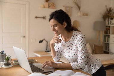 Gülümseyen kadın evde bilgisayar kullanıyor, çalışıyor ya da çalışıyor.