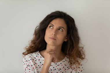 Düşünceli bir kadın çenesine dokunuyor, düşüncelere dalmış.