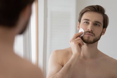 Çekici metroseksüel adam yüzünü pamuk diskle temizliyor.