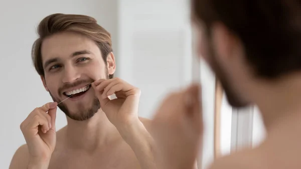 Happy handsome young guy cleaning white teeth with floss — Stock Photo, Image