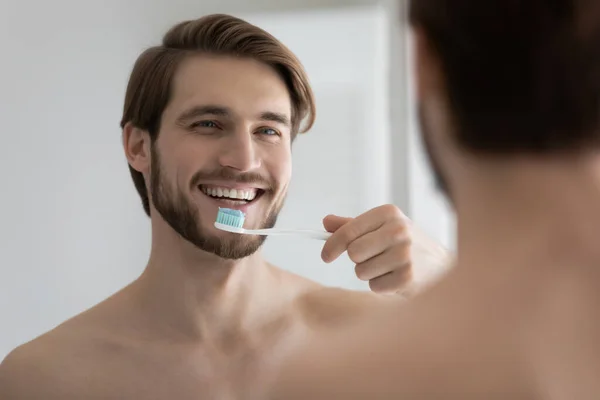 Heureux jeune homme attrayant brossant des dents saines dans la salle de bain — Photo