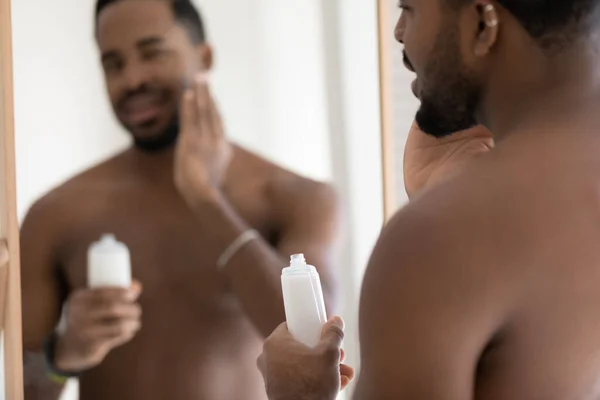 Handsome muscular mixed race Black young man applying aftershave lotion — Stock Photo, Image