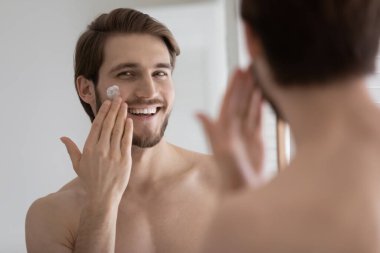 Mutlu, rahat, yakışıklı genç adam kolajen kremi sürüyor.