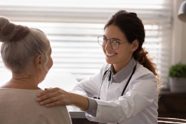 Gülümseyen doktor klinikteki yaşlı kadına destek oluyor.