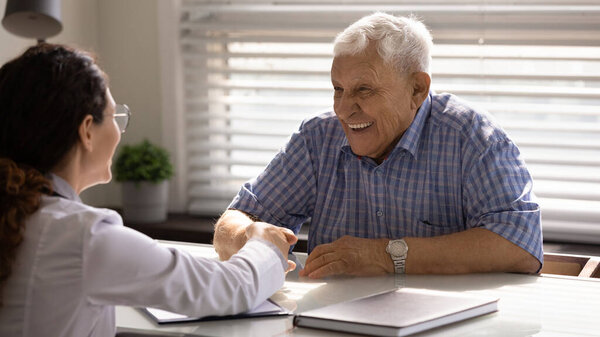 Женщина-врач пожимает руку, улыбаясь зрелому пациенту