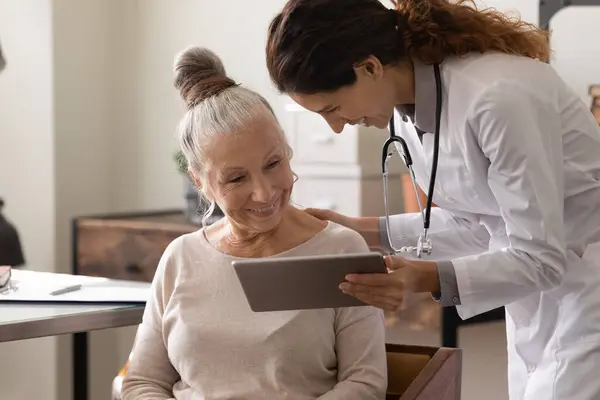 Женщина врач использовать таблетки на консультации со зрелым пациентом — стоковое фото