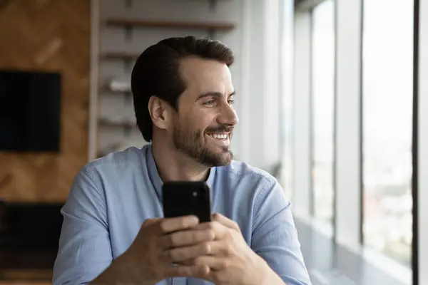 Soñador joven feliz hombre sosteniendo teléfono inteligente en las manos. —  Fotos de Stock